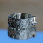 Silver textured ring on a reflective surface with a blurred background