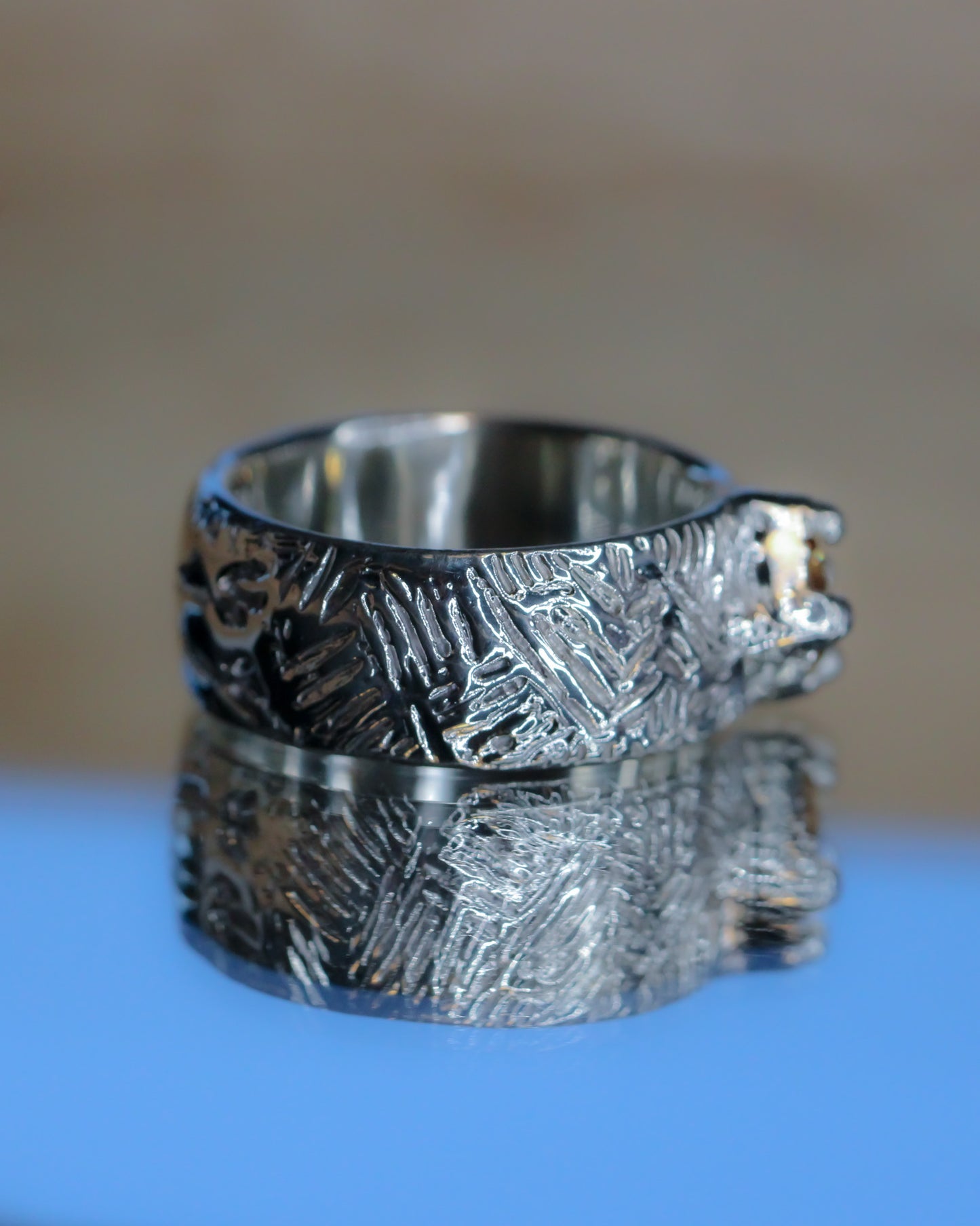 Silver textured ring on a reflective surface with a blurred background