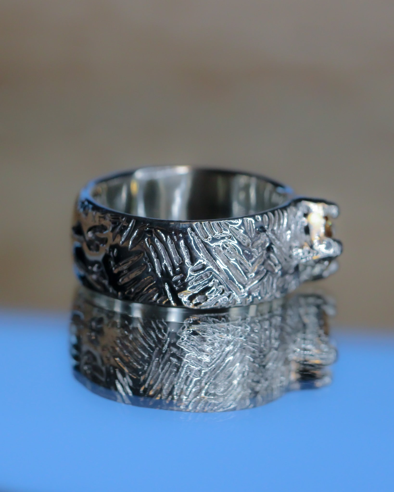 Silver textured ring on a reflective surface with a blurred background