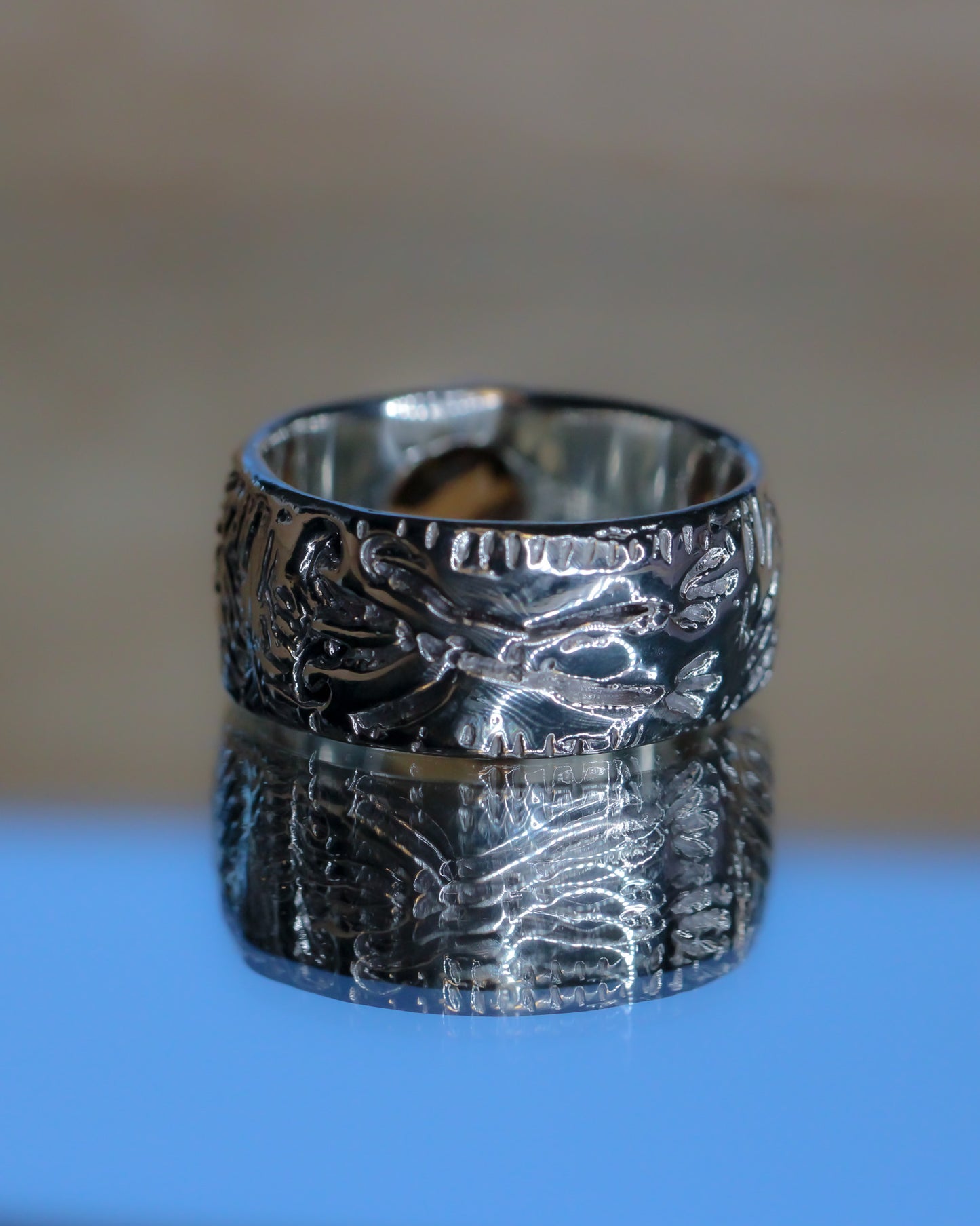 Silver ring with intricate design on a reflective surface